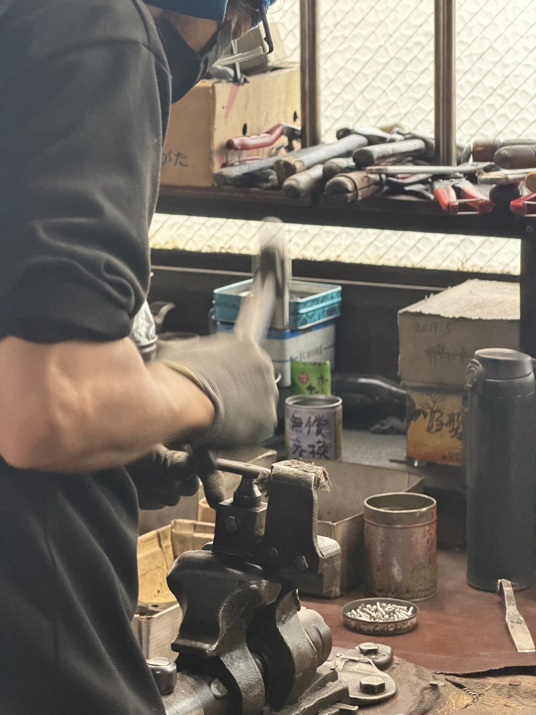 A gloved hand striking a piece held in a vise